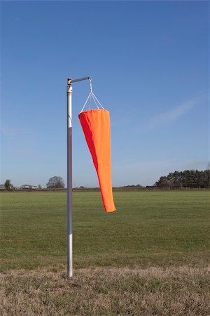 landscape with a bright orange wind sock on a rural grass airstrip moves slightly in a light breeze under a blue sky Fotografie stock - Microstock e Abbonamento, Codice: 400-06067774