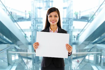 simsearch:400-06071690,k - Mixed race Asian businesswoman holding a white board standing inside modern building. Photographie de stock - Aubaine LD & Abonnement, Code: 400-06087203