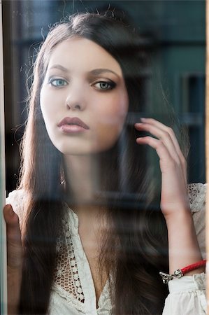 Portrait of a lovely young lady looking through glass window - Indoor in a dark cloudy day, she is in front of the camera and has the left hand near the hair Stock Photo - Budget Royalty-Free & Subscription, Code: 400-06087321