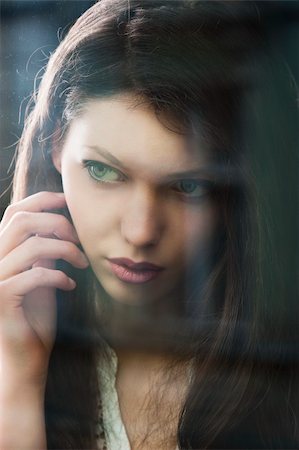 Portrait of a lovely young lady looking through glass window - Indoor in a dark cloudy day, she looks at right and has the right hand near the face Stock Photo - Budget Royalty-Free & Subscription, Code: 400-06087322