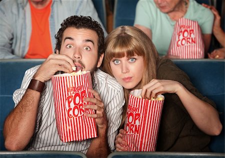 suspense - Captivated couple  with popcorn bags in a theater Fotografie stock - Microstock e Abbonamento, Codice: 400-06104102