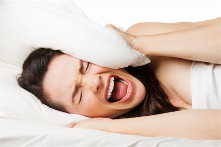 A frustrated tired woman hides her head in her pillow and screams beacuse she can't sleep. Isolated on white. Photographie de stock - Aubaine LD & Abonnement, Code: 400-06108679