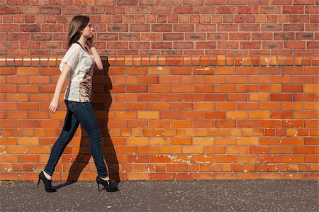 Young woman walk beside the red brick wall while  talking on the phone Stock Photo - Budget Royalty-Free & Subscription, Code: 400-06100318