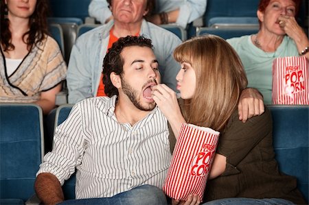 photo of a woman feeding her husband food - Loving young girlfriend feeds boyfriend popcorn in a theater Stock Photo - Budget Royalty-Free & Subscription, Code: 400-06138373