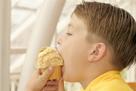 Child taking a bite of a muffin in cafeteria. Stock Photo - Budget Royalty-Free & Subscription, Code: 400-06131035