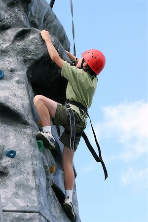 foothold - Boy climbing and stretching and nearly at the summit, on a training rock face, wearing a harness and red hard hat. Photographie de stock - Aubaine LD & Abonnement, Code: 400-06131202