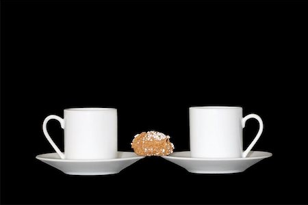 Two white china espresso coffee cups and saucers with a sugar coated biscuit linking the two, against a black background. Stock Photo - Budget Royalty-Free & Subscription, Code: 400-06133560