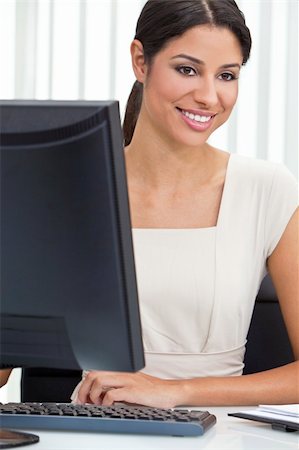 smiling young latina models - Beautiful young Latina Hispanic woman or businesswoman in smart business suit sitting at a desk in an office using a computer Foto de stock - Super Valor sin royalties y Suscripción, Código: 400-06140757
