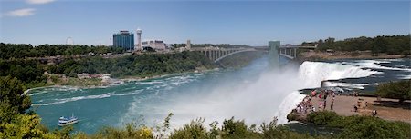 A shot of the American Falls from Goat Island. Image shows the falls, observation platform / elevator to the bottom of the Lewiston Gorge, Rainbow Bridge and parts of Niagara Falls, New York and Ontario. The maid of the mist is in the foreground heading toward the Horseshoe Falls. Foto de stock - Super Valor sin royalties y Suscripción, Código: 400-06179865