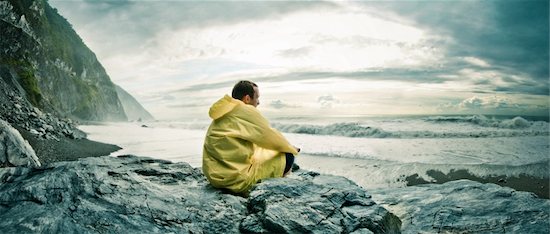 Young man sitting on a rock on a rocky beach watching the ocean in a yellow rain coat. Location: Hualien County, Taiwan Foto de stock - Sin royalties, Artista: Alan_Smithee, Código de la imagen: 400-06205623