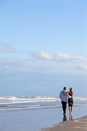simsearch:400-06751687,k - A young man and woman romantic couple walking embracing on a beach with a bright blue sky Stock Photo - Budget Royalty-Free & Subscription, Code: 400-06333471