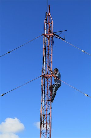 Radio tower or mast, with a worker climbing up it beneath blue sky and copy space. Foto de stock - Super Valor sin royalties y Suscripción, Código: 400-06364052