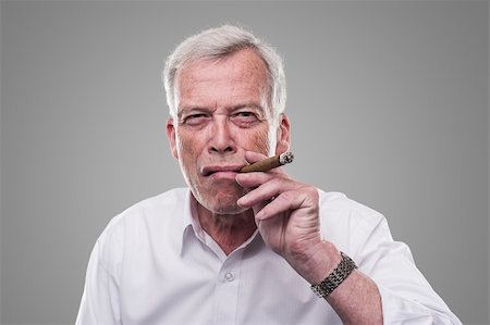 Handsome senior man with a shrewd expression and strong personaity smoking a cigar isolated on a grey studio background Stock Photo - Budget Royalty-Free & Subscription, Code: 400-06361005