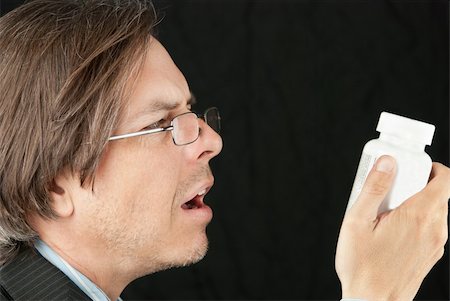 Close-up of a casual businessman wearing glasses trying to read a pill bottle label. Stock Photo - Budget Royalty-Free & Subscription, Code: 400-06393243