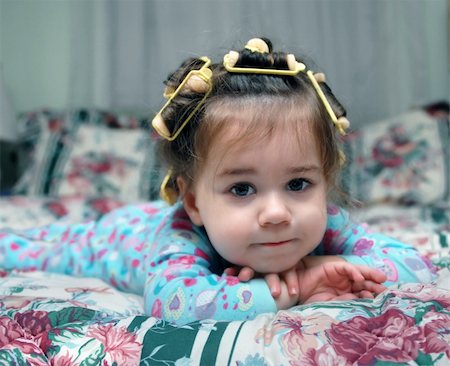 Toddler lays on her bed wearing pajamas and hair curlers.  She is leaning her head on her hands and is lost in thought. Foto de stock - Royalty-Free Super Valor e Assinatura, Número: 400-06413050