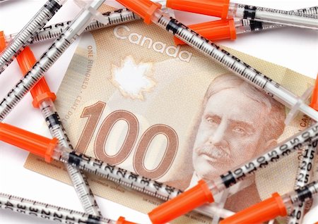 A one hundred dollar Canadian bill covered by medical syringes isolated on white. Stock Photo - Budget Royalty-Free & Subscription, Code: 400-06425280