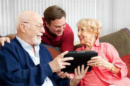 Senior couple get a gift of a tablet PC from their adult son. Foto de stock - Super Valor sin royalties y Suscripción, Código: 400-06420506