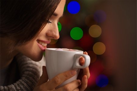 Happy young woman enjoying cup of hot beverage in front of Christmas lights Stock Photo - Budget Royalty-Free & Subscription, Code: 400-06458846