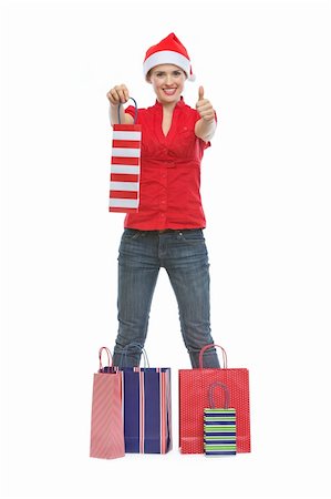 Happy young woman in Christmas hat standing among shopping bags and showing thumbs up Stock Photo - Budget Royalty-Free & Subscription, Code: 400-06458868