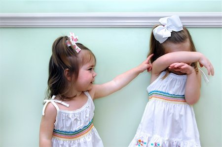 Baby sister teases older sister with an accusing finger.  Big sister covers her head upset and distressed. Foto de stock - Royalty-Free Super Valor e Assinatura, Número: 400-06461369