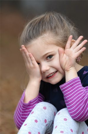 Small child is afraid to look as she peaps out from behind her hand.  She is sitting outdoors in a colorful purple striped shirt. Foto de stock - Royalty-Free Super Valor e Assinatura, Número: 400-06461370