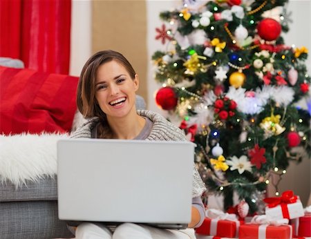 Smiling young woman with laptop sitting near Christmas tree Foto de stock - Super Valor sin royalties y Suscripción, Código: 400-06463695