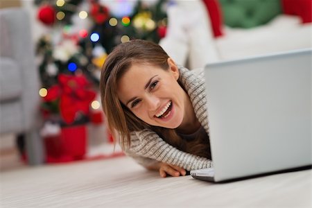 Smiling woman looking out from laptop in front of Christmas tree Stock Photo - Budget Royalty-Free & Subscription, Code: 400-06484203