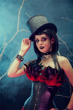 simsearch:400-07776243,k - Attractive smiling gothic girl in tophat and feather corset, studio shot with fog and branches Fotografie stock - Microstock e Abbonamento, Codice: 400-06518923