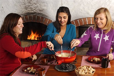 Photo of three beautiful females dipping bread into the melted cheese in a fondue pot. Stock Photo - Budget Royalty-Free & Subscription, Code: 400-06524453