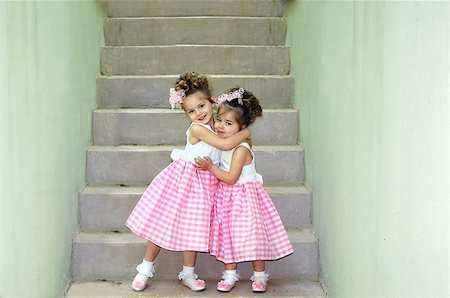 Two sisters hug affectionately at the bottom of a flight of concrete steps.  They are dressed identically and ready for Easter Sunday morning at Church. Foto de stock - Royalty-Free Super Valor e Assinatura, Número: 400-06526243