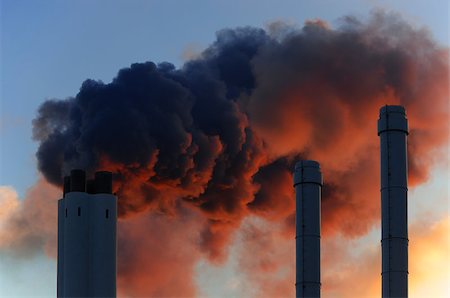 Pollution concept of smoking chimneys. The setting sun illuminates the vapor from below, giving it an ominous impression, like that of volcano smoke. Stockbilder - Microstock & Abonnement, Bildnummer: 400-06565957