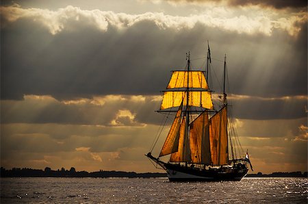 A three-master sailing on the Elbe near Hamburg. The evening light breaks through the gaps in the clouds behind the ship, illuminating the sails from behind. Processed to give it an antique look. Foto de stock - Royalty-Free Super Valor e Assinatura, Número: 400-06565958