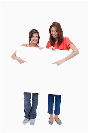 simsearch:400-06634629,k - Teenagers smiling and standing behind a blank poster while pointing it Fotografie stock - Microstock e Abbonamento, Codice: 400-06634645