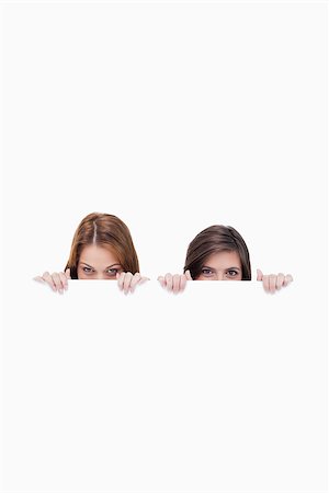 simsearch:400-06634629,k - Two friends secretly hiding behind a blank poster against a white background Fotografie stock - Microstock e Abbonamento, Codice: 400-06634877