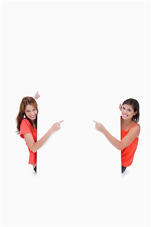 simsearch:400-06634629,k - Teenagers cutely looking at the camera and pointing their fingers on a blank poster Fotografie stock - Microstock e Abbonamento, Codice: 400-06634882