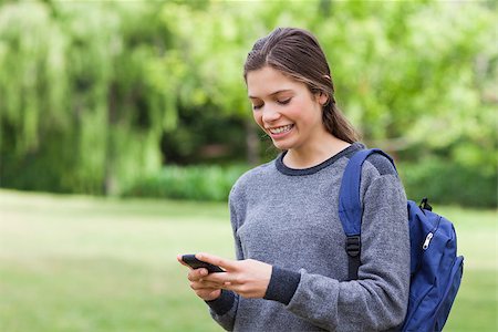 Smiling teenage girl receiving a text with her cellphone while standing in a park Stock Photo - Budget Royalty-Free & Subscription, Code: 400-06635320