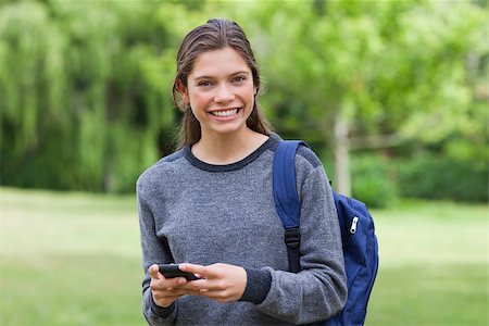 Young smiling woman looking straight at the camera while using her mobile phone Stock Photo - Budget Royalty-Free & Subscription, Code: 400-06635321