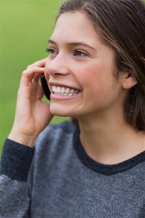 Young smiling girl using her mobile phone while standing upright in a park Stock Photo - Budget Royalty-Free & Subscription, Code: 400-06635323