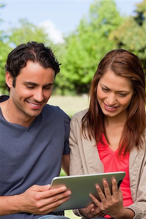 Man and his friend smiling as the watch something on a tablet in a sunny park Stock Photo - Budget Royalty-Free & Subscription, Code: 400-06635461