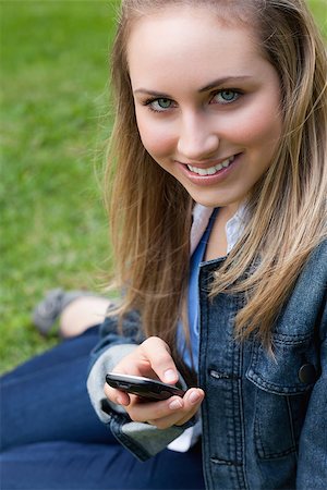 Young blonde girl sitting on the grass in a park while sending a text with her cellphone Stock Photo - Budget Royalty-Free & Subscription, Code: 400-06635636