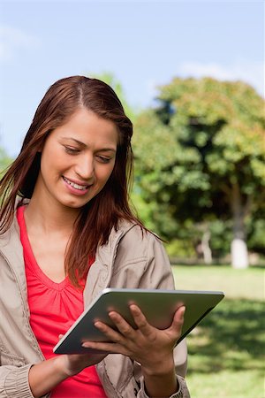 students tablets outside - Young woman smiling while using a tablet and standing in bright park Stock Photo - Budget Royalty-Free & Subscription, Code: 400-06635683