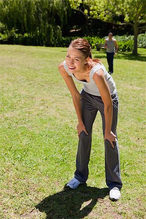 Woman smiling as she bends over recovering while a man is walking towards her in the background Stock Photo - Budget Royalty-Free & Subscription, Code: 400-06635750