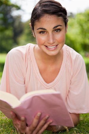 Woman looking ahead and smiling while reading a book as she is lies in grass with trees in the background Stock Photo - Budget Royalty-Free & Subscription, Code: 400-06635784
