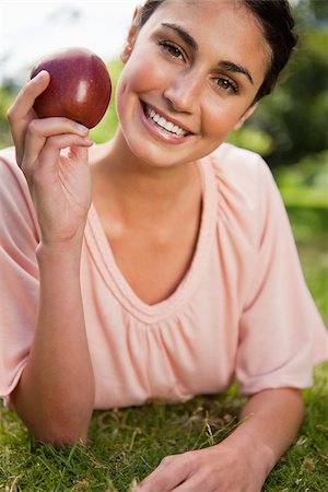 portrait of woman with fruit on head - Woman smiles while holding a red apple as she is lying prone in grass Photographie de stock - Aubaine LD & Abonnement, Code: 400-06635788