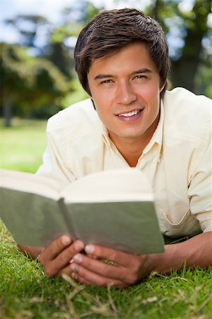 Man looking straight ahead of him and smiling while reading a book as he lies on grass Stock Photo - Budget Royalty-Free & Subscription, Code: 400-06635782