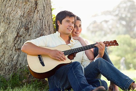 Man and his friend look into the distance as they listen to him playing the guitar while sitting against the trunk of a tree Foto de stock - Super Valor sin royalties y Suscripción, Código: 400-06635934