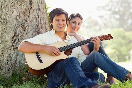 Man and his friend look straight ahead as they listen to him playing the guitar while sitting against the trunk of a tree Stock Photo - Budget Royalty-Free & Subscription, Code: 400-06635935