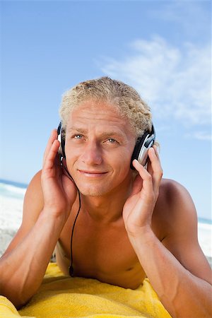 Smiling young man lying on the beach while listening to music in his headset Stock Photo - Budget Royalty-Free & Subscription, Code: 400-06636070