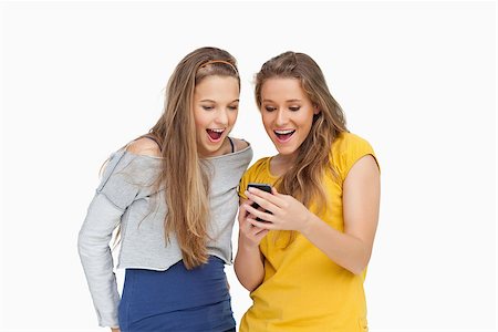 Two voiceless young women looking a smartphone against white background Stock Photo - Budget Royalty-Free & Subscription, Code: 400-06637935