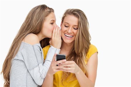 Young woman whispering to her friend who's texting on her phone against white background Stock Photo - Budget Royalty-Free & Subscription, Code: 400-06637940
